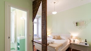Un dormitorio con cama, mesita de noche, lámpara y un espejo en la pared.