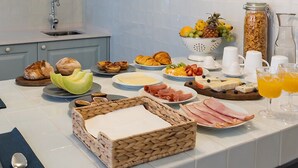 Una cocina con armarios azul claro, encimera blanca y diversos alimentos para el desayuno, incluyendo pan, pasteles, frutas y bebidas.