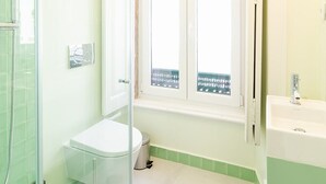 Un baño con cabina de ducha de vidrio, inodoro, lavamanos y ventana con vistas.