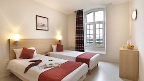 A hotel room with two beds, a window with curtains, a bedside table with a fruit bowl, and a wall-mounted picture. - Vacancéole - Les Demeures Champenoises (Epernay)