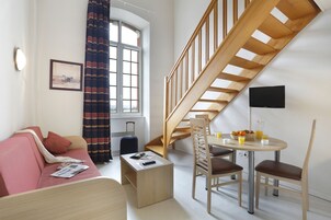 Una habitación moderna con una escalera de madera, un sofá, una pequeña mesa con sillas y un ventanal con cortinas.