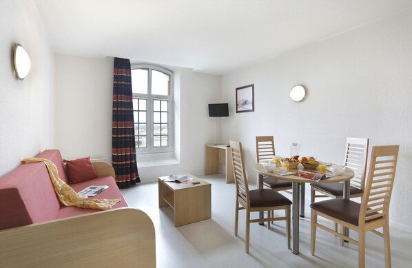 A modern living room with a sofa, a dining table with chairs, a small coffee table, and a TV on a stand. - Vacancéole - Les Demeures Champenoises (Epernay)