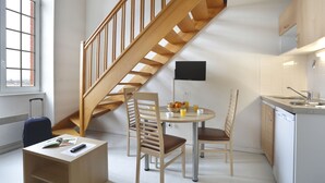 A compact kitchen with a wooden staircase, a dining table with chairs, a small island with a sink, and a suitcase in the corner. - Vacancéole - Les Demeures Champenoises (Epernay)
