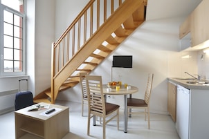 Una cocina compacta con una escalera de madera, una mesa de comedor con sillas, una pequeña isla con un fregadero y una maleta en la esquina.