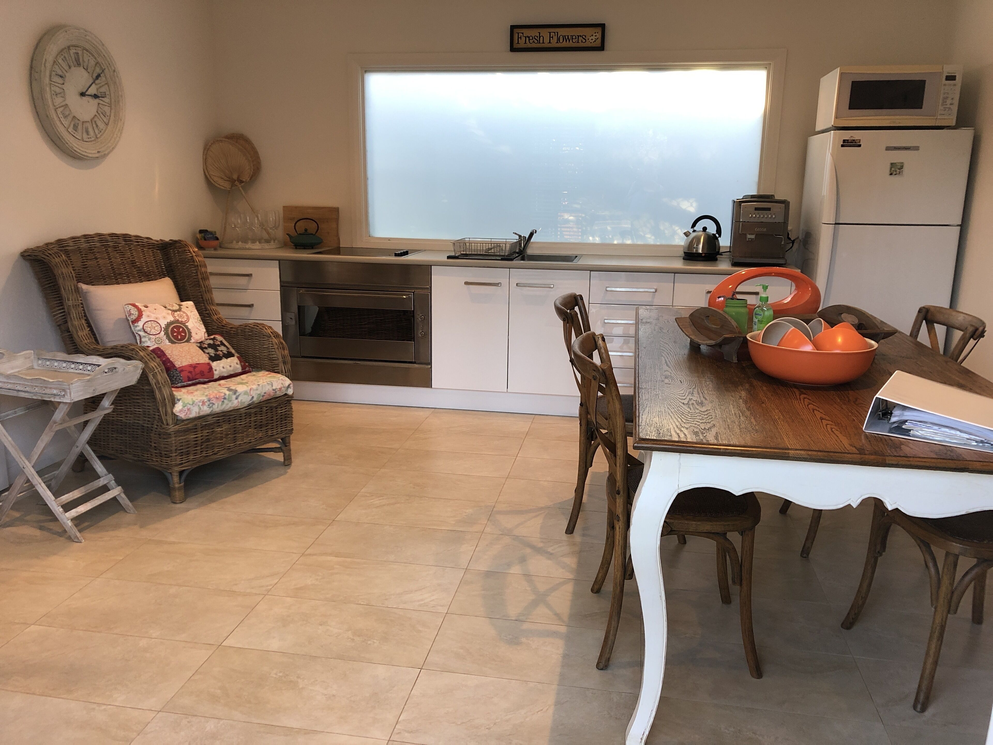A kitchen with a dining area, a wicker chair, a table with a bowl, and a refrigerator.