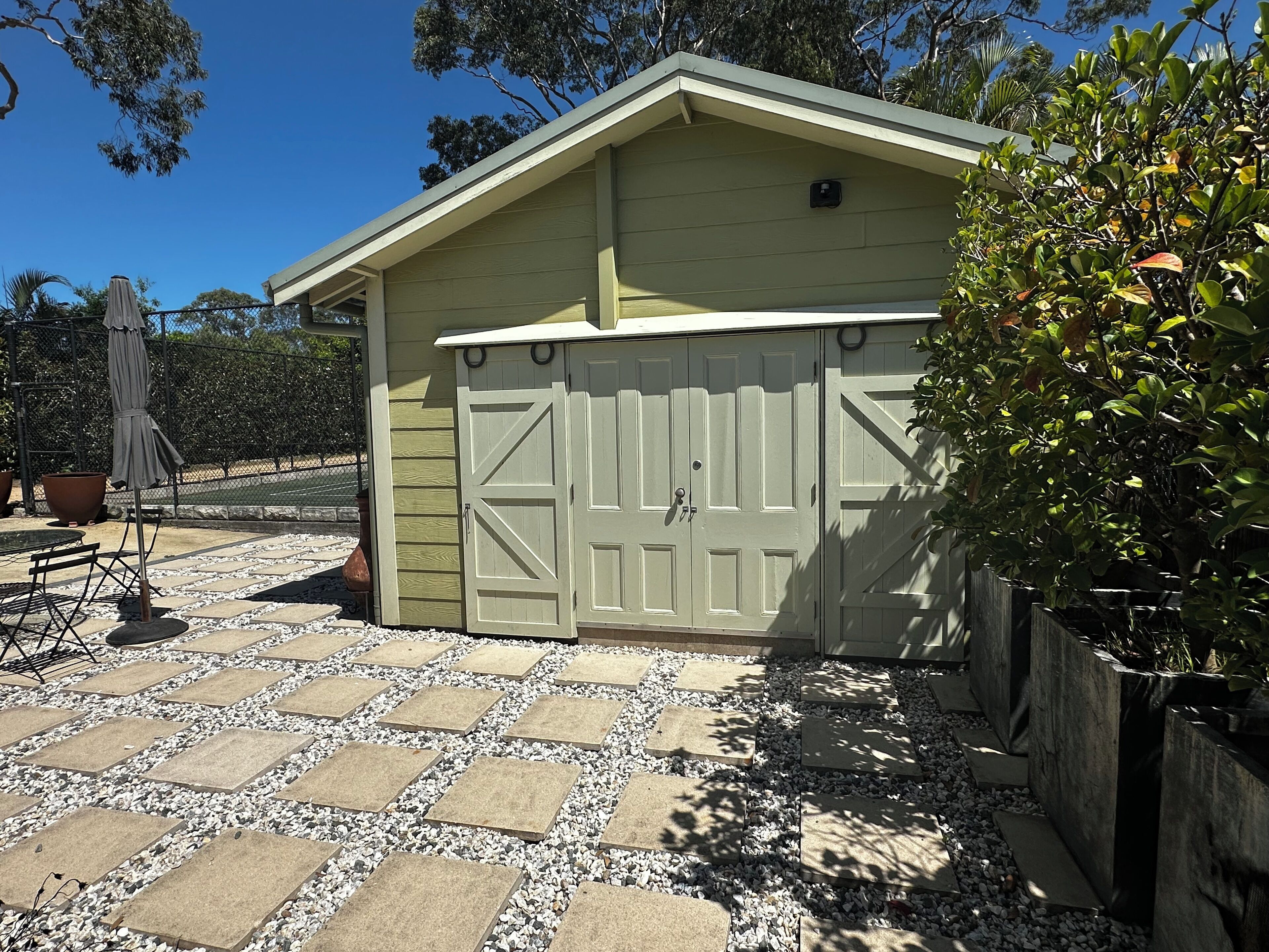 Eine Garage mit weißer Tür, eine Terrasse mit Steinplatten und ein Zaun.
