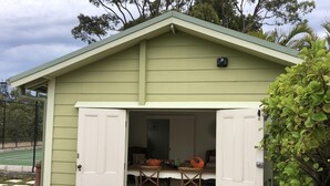 Un cobertizo verde con puertas blancas, una mesa y dos sillas en su interior.