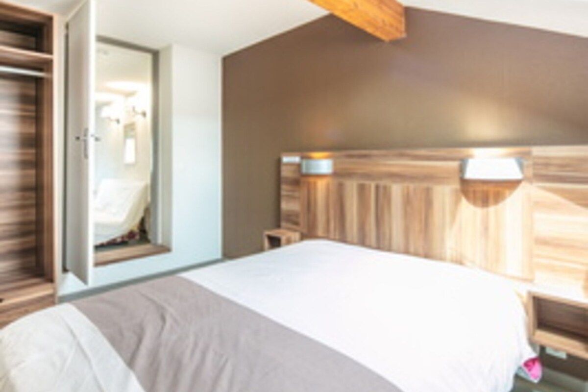 Une chambre à coucher comprenant un lit, une table de chevet, une tête de lit en bois et une porte donnant sur une salle de bain.