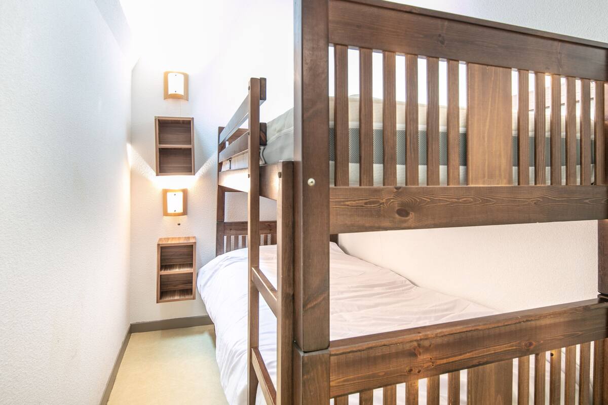 A bunk bed with a wooden headboard, a bedside table, and a wall-mounted shelf with a light.