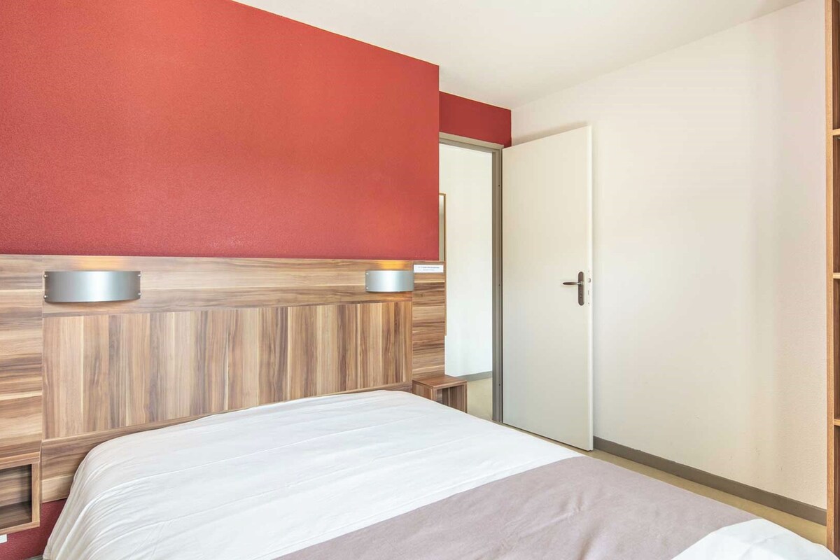 Habitación de hotel con una cama, cabecera de madera, pared de acento roja y puerta blanca.
