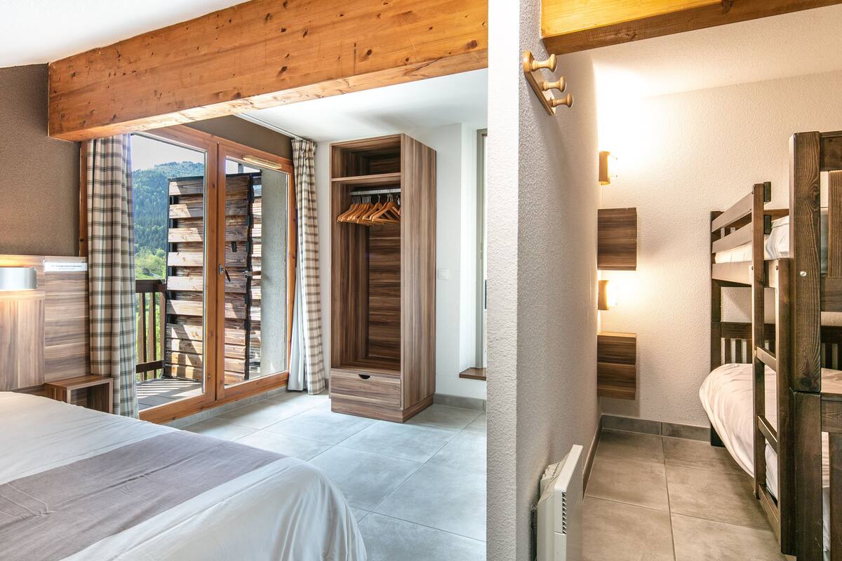A bedroom with a bed, a wooden wardrobe, a radiator, and a view of the outdoors.