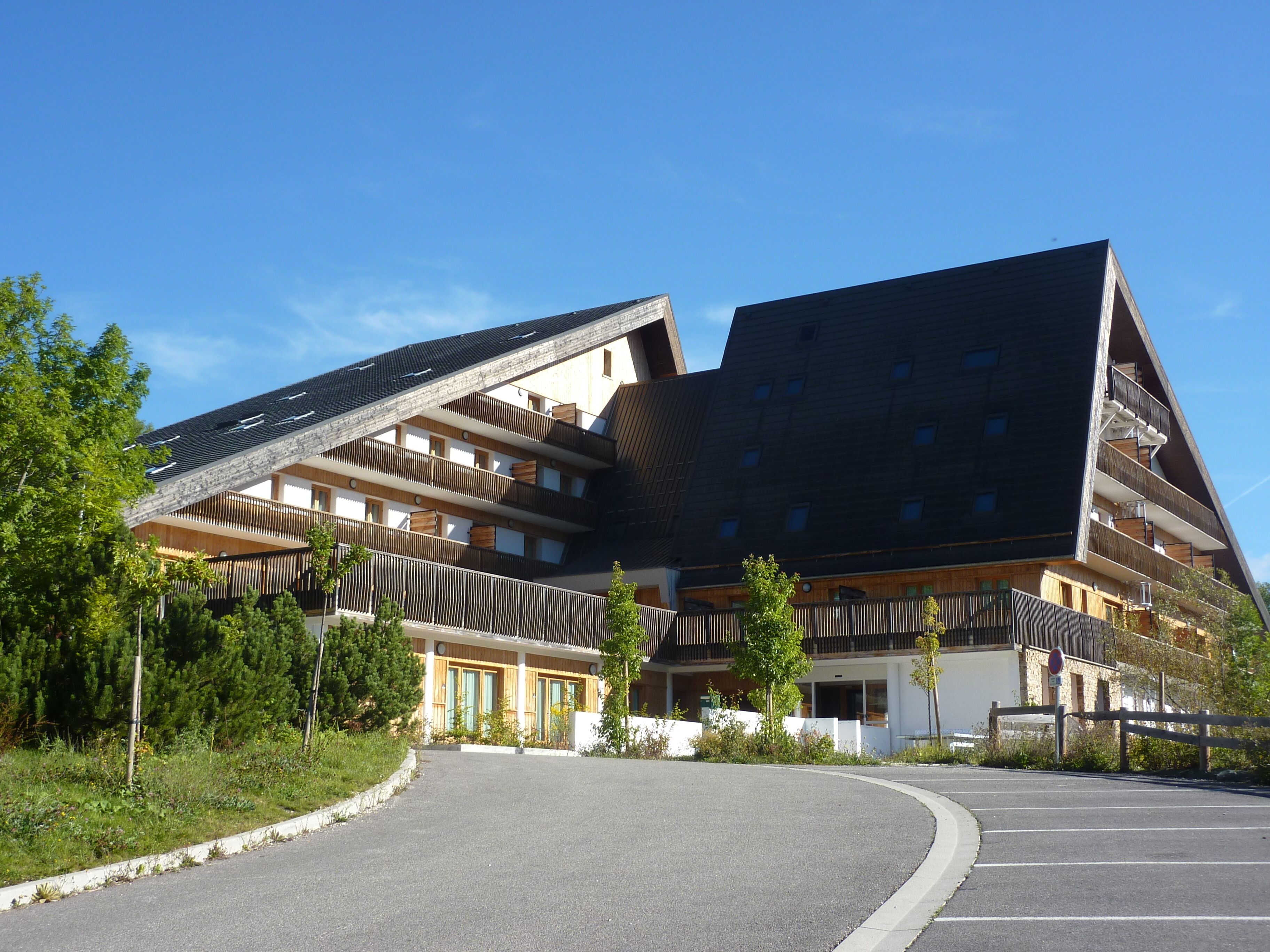 Un immeuble moderne à plusieurs étages, doté d’un toit en pente, de balcons et d’un espace de stationnement.