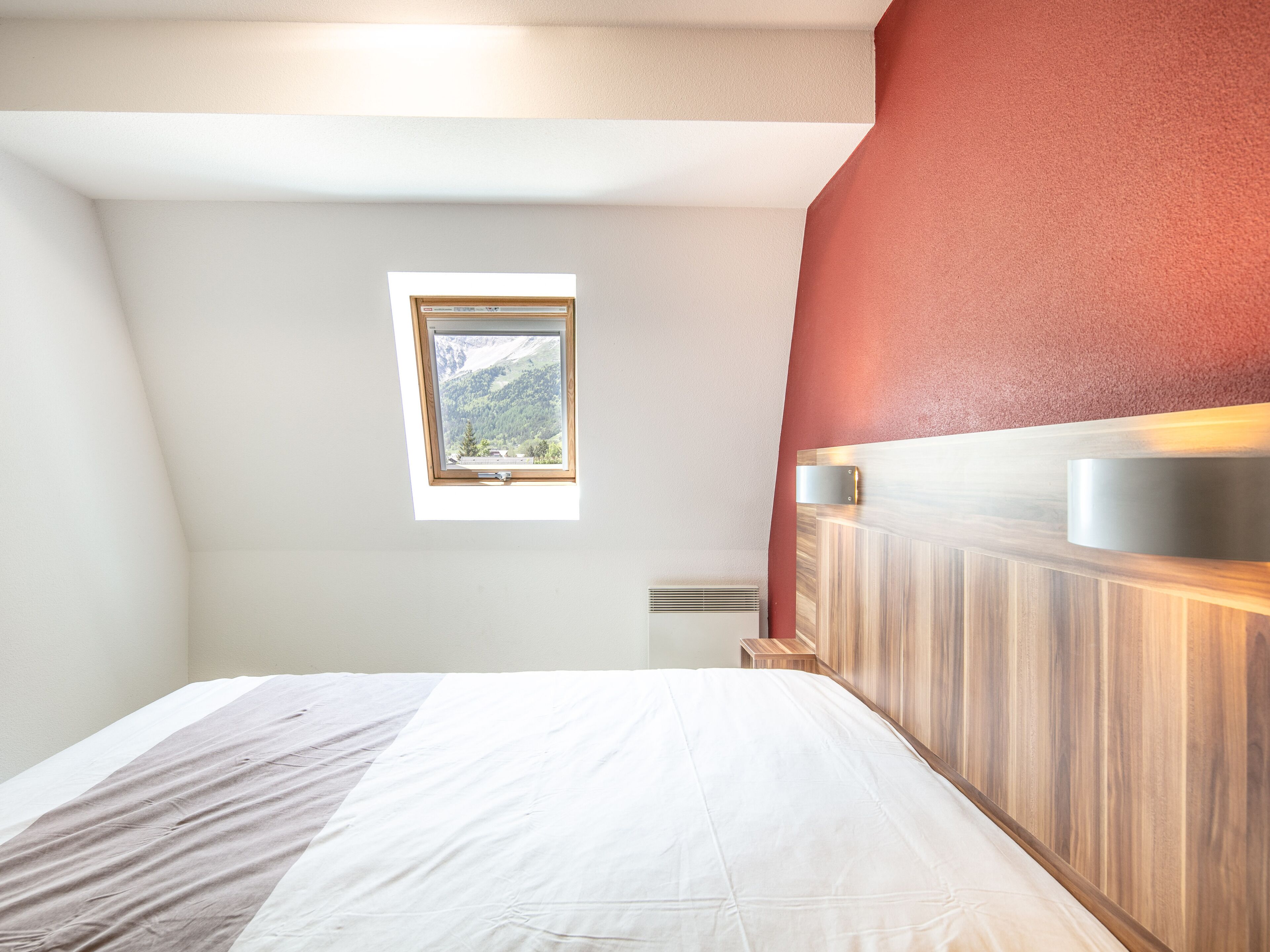 Une chambre à coucher avec un lit, une fenêtre, une tête de lit en bois et une petite table de chevet.