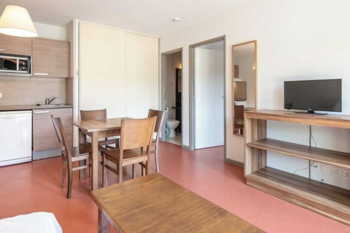 Un espace de vie compact comprenant un coin cuisine, un coin repas, un téléviseur et un miroir.