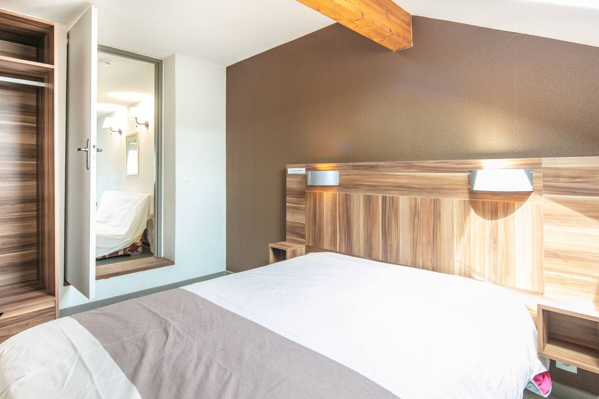 A bedroom with a bed, a wooden headboard, a bedside table, and a mirror.