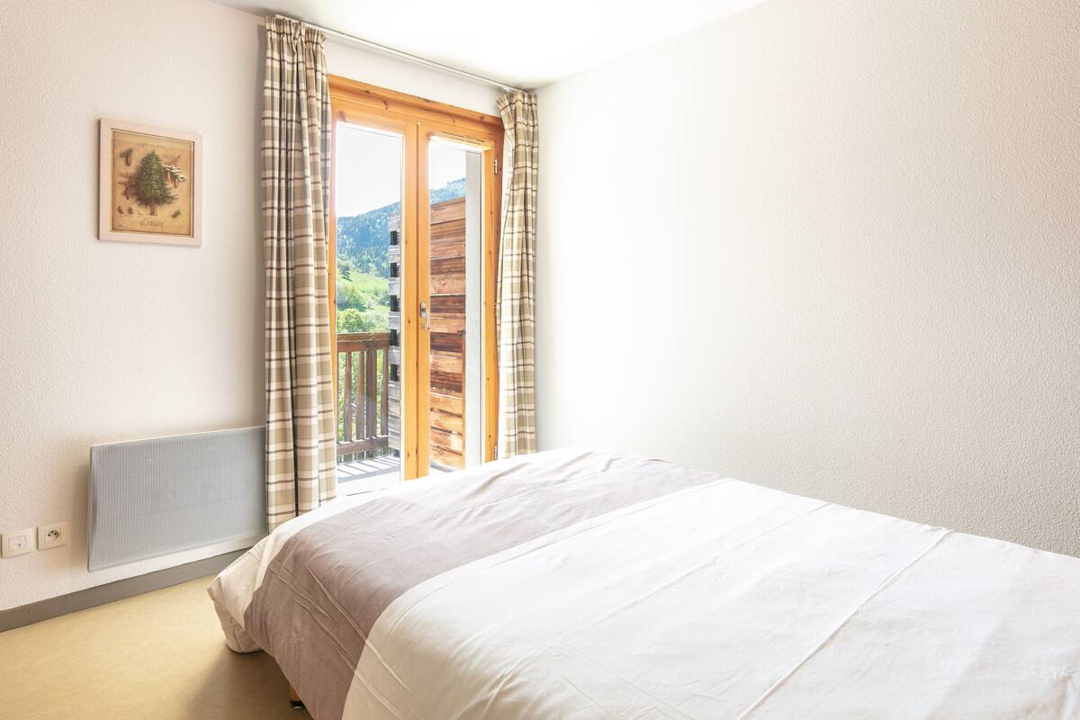 A bedroom with a bed, a window with curtains, a radiator, and a framed picture on the wall.