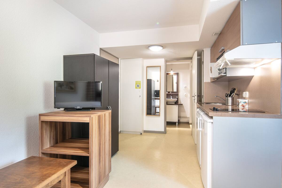 A compact kitchen with a built-in TV, a small dining table, and a refrigerator.