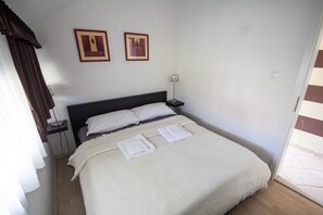 A neatly made bed with two pillows and two folded towels, a bedside table with a lamp, and two framed pictures on the wall.