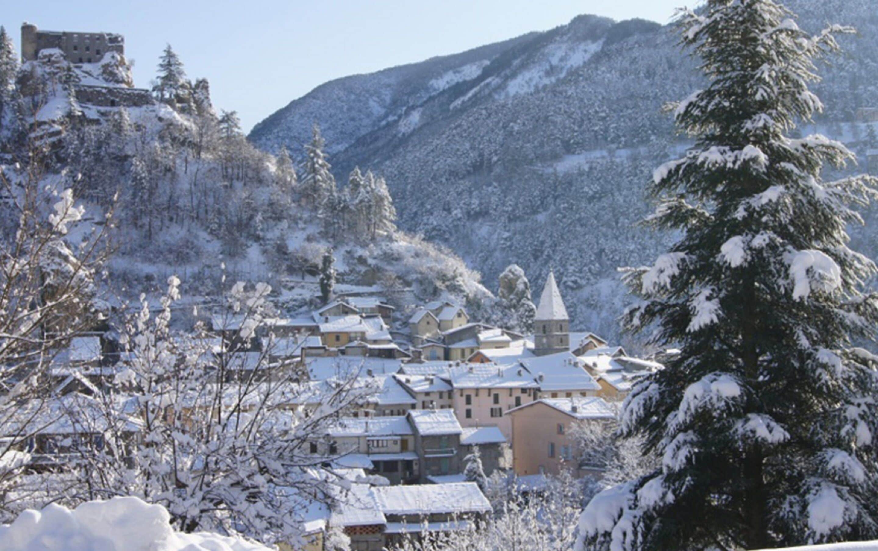 A snow-covered village with buildings clustered together, surrounded by mountains.