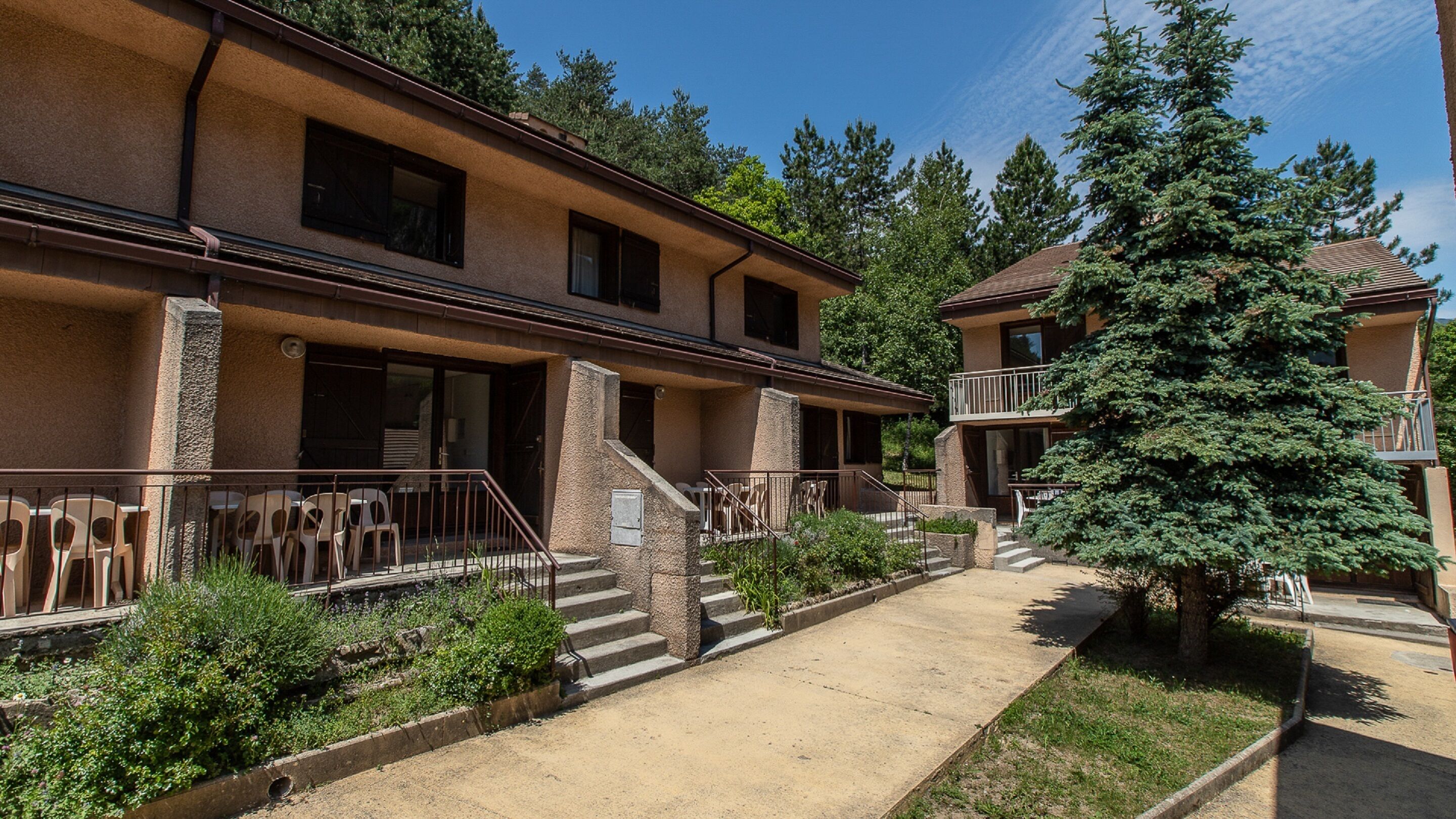 A two-story building with a stone facade, multiple balconies, and a well-maintained garden area.