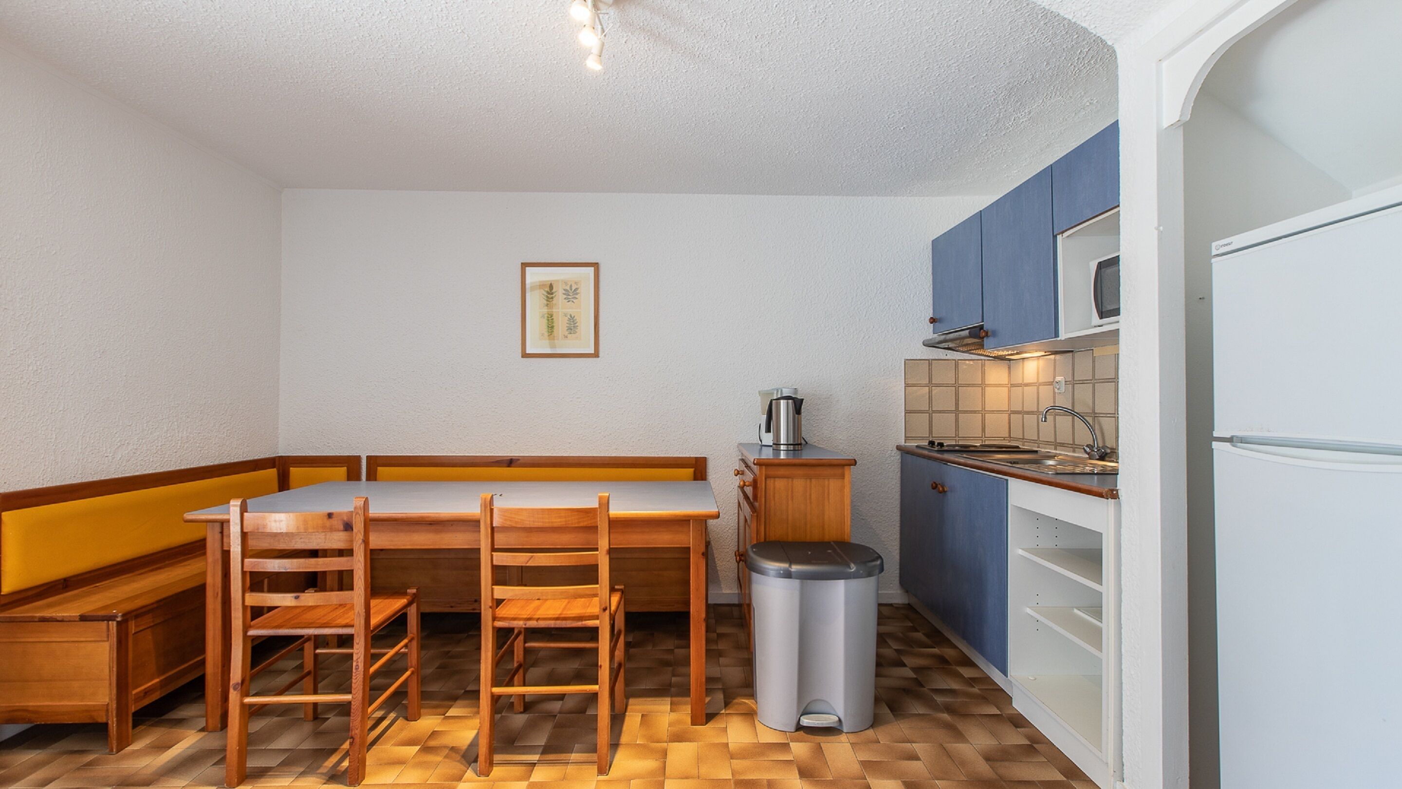 Une cuisine compacte avec une table à manger en bois, des chaises, une poubelle et une cuisinière intégrée.
