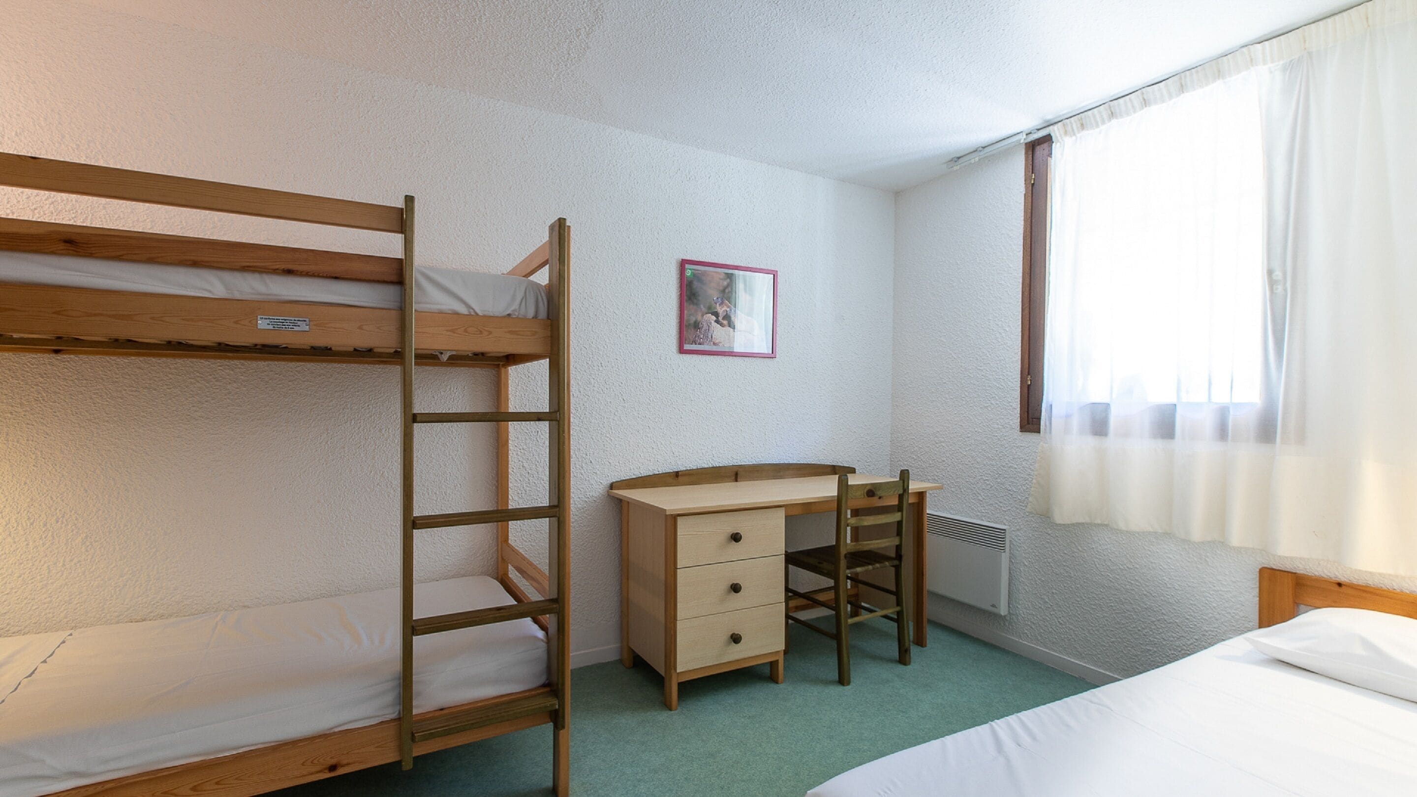 Una cama litera con escalera, un escritorio con cajones, una silla y un radiador.
