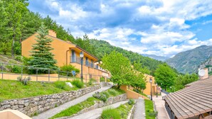 A hillside residential area with stone steps leading to a building with balconies, surrounded by greenery and mountains in the background. - Vacancéole - Résidence Les Gorges Rouges (Guillaumes)
