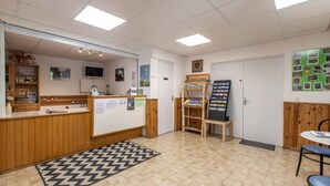 A reception area with a wooden counter, a bulletin board, a small table, and a patterned rug. - Vacancéole - Résidence Les Gorges Rouges (Guillaumes)