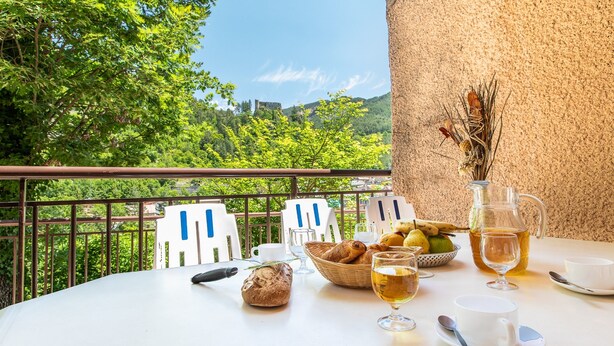 A table set with bread, pastries, fruit, wine, and a vase with dried flowers, overlooking a scenic landscape. - Vacancéole - Résidence Les Gorges Rouges (Guillaumes)
