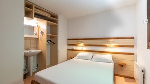 A bedroom with a bed, bedside table, and a built-in wardrobe with a mirror and hanging clothes. - Vacancéole - Résidence Les Gorges Rouges (Guillaumes)