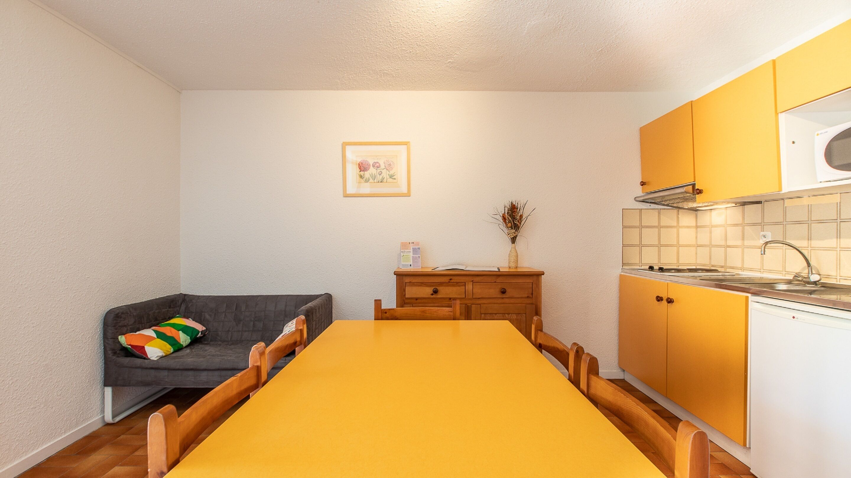 A compact kitchen with a dining table, a sofa, and a cabinet.
