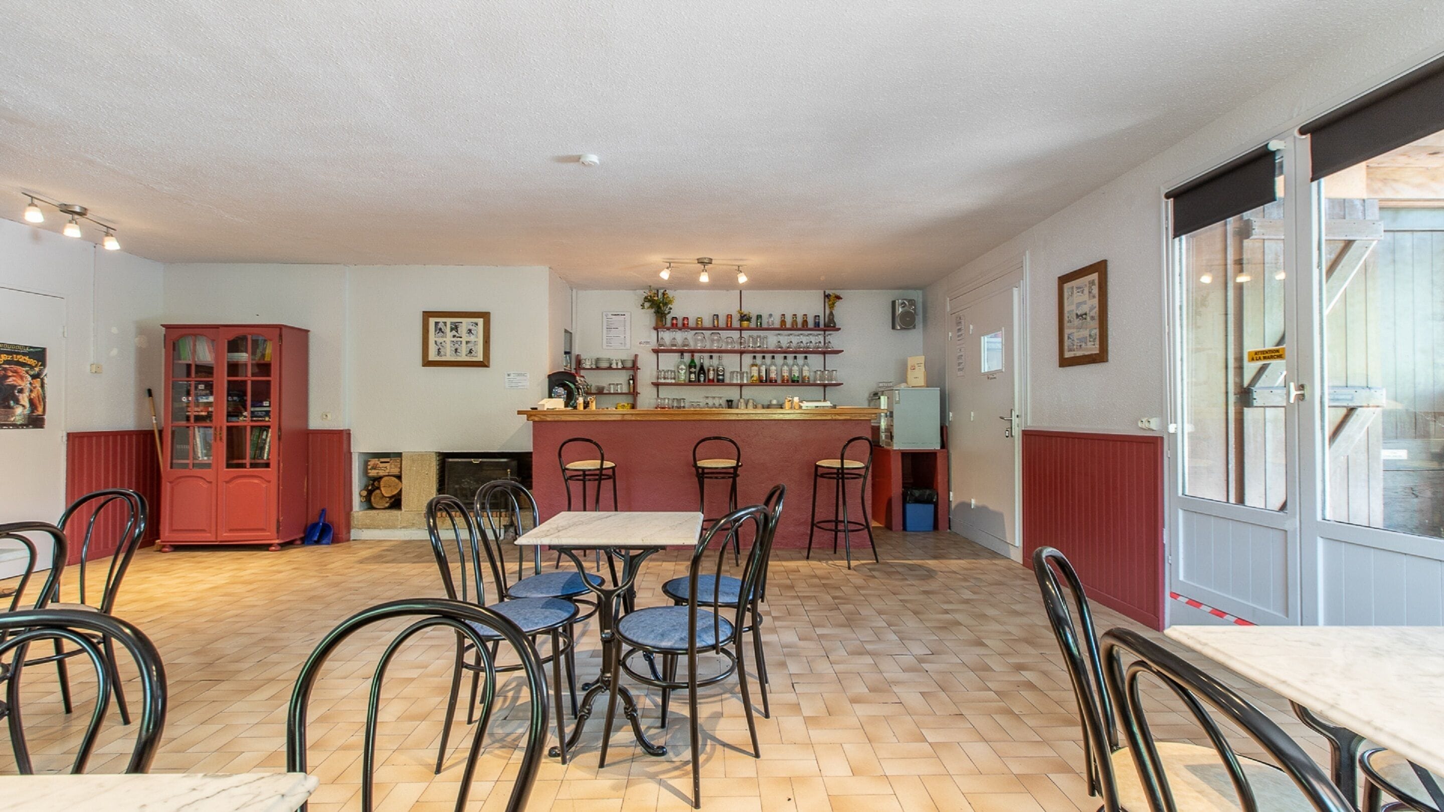 Un restaurante con zona de bar, suelo de madera y sillas metálicas.