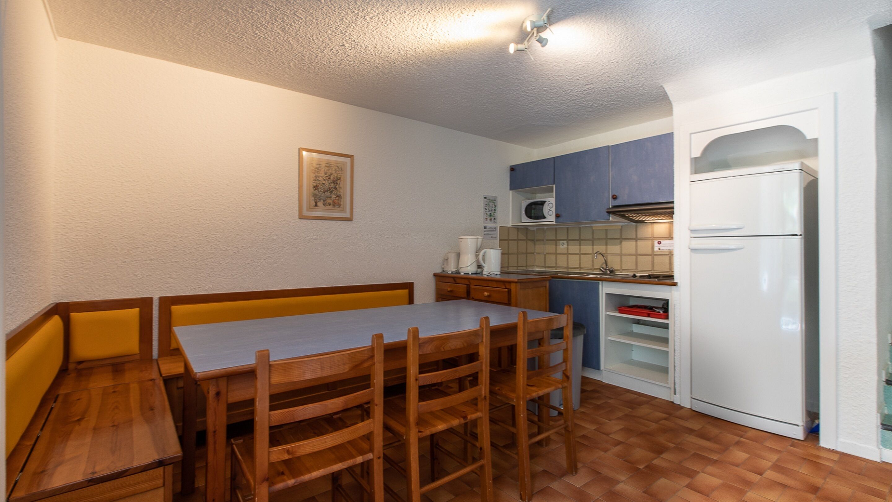 A compact kitchen with a wooden dining table and chairs, a microwave, and a white refrigerator.