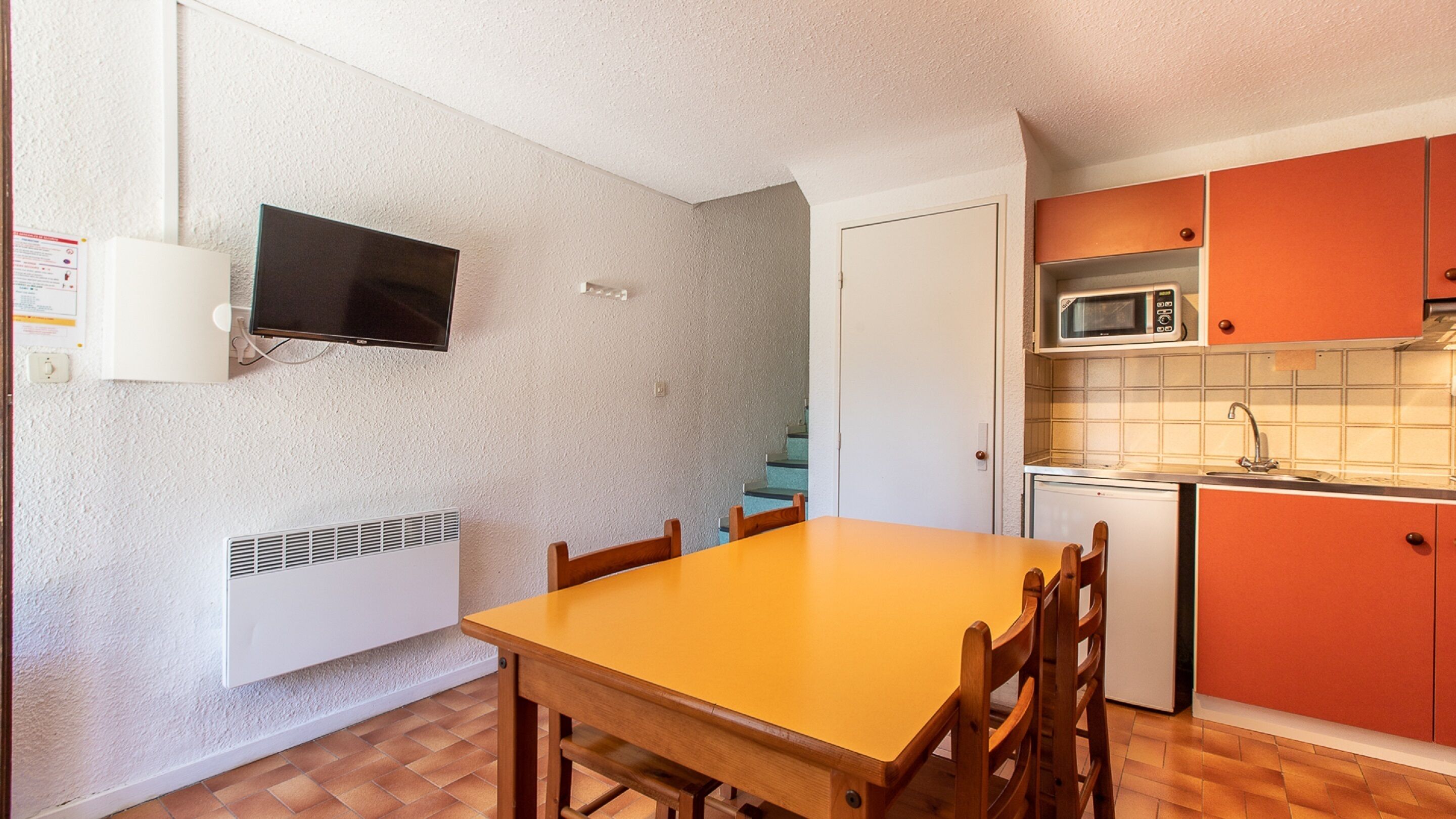 Una cocina compacta con una mesa y sillas de madera, un microondas y un refrigerador pequeño.