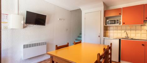Una cocina compacta con una mesa y sillas de madera, un microondas y un refrigerador pequeño.