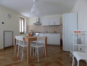 Une cuisine avec une table en bois et des chaises blanches, un réfrigérateur blanc et un mur recouvert de carreaux.