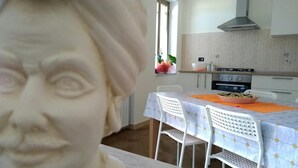 A dining area with a table set for two, a kitchen in the background, and a window with a plant. - Pergusa Lake Home (Enna)