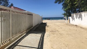 Un sendero que lleva a una playa, con una cerca blanca a un lado y un cielo azul despejado.