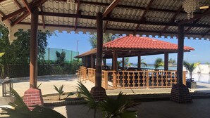 Un espacio al aire libre cubierto con techo de tejas rojas, bancos de madera y vistas a la playa.