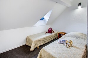 A small, well-lit room with two beds, a red backpack, and a book on one bed.
