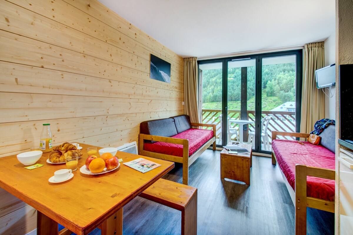 A wooden-paneled room with a dining table set with breakfast items, a sofa, and a bed.