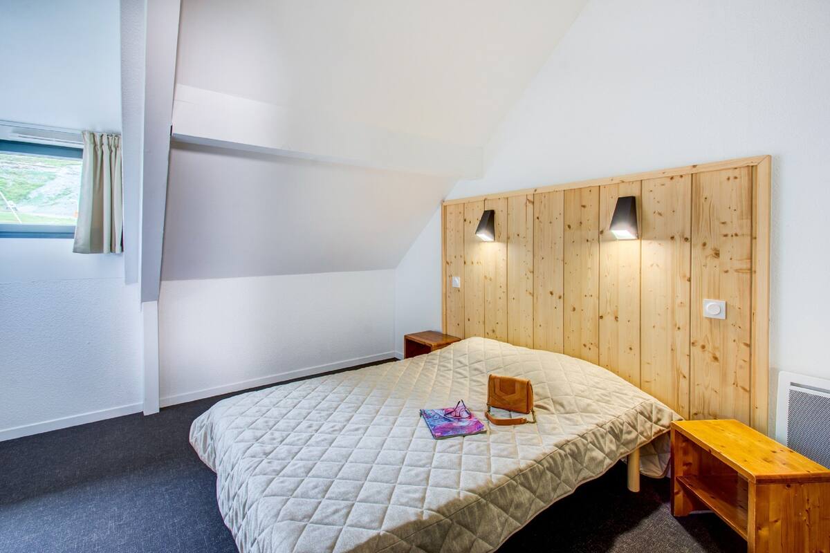 A bedroom with a wooden headboard, a bed with a quilted bedspread, a bedside table, and a nightstand.