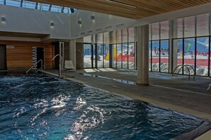 An indoor swimming pool with a view of an outdoor snowy area.