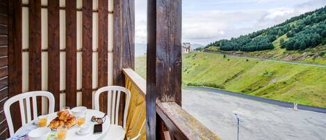 A balcony with a table set for breakfast, overlooking a road and green hills.