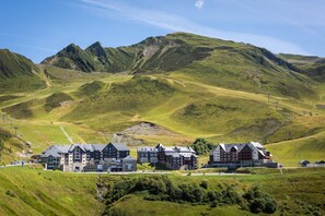 A hotel with multiple buildings, set in a hilly landscape with mountains in the background.