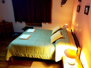 A neatly made bed with pillows and a blanket, a bedside table with a lamp, and a window with curtains. - Hospedaje La Nuit (Cusco)