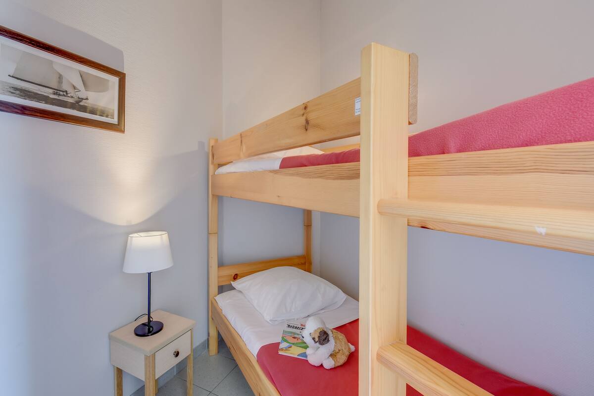 A bunk bed with a red mattress, a small bedside table with a lamp, and a framed picture on the wall.