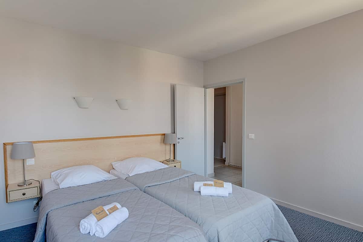 A hotel room with two beds, each with a headboard, bedside lamps, and neatly folded towels.