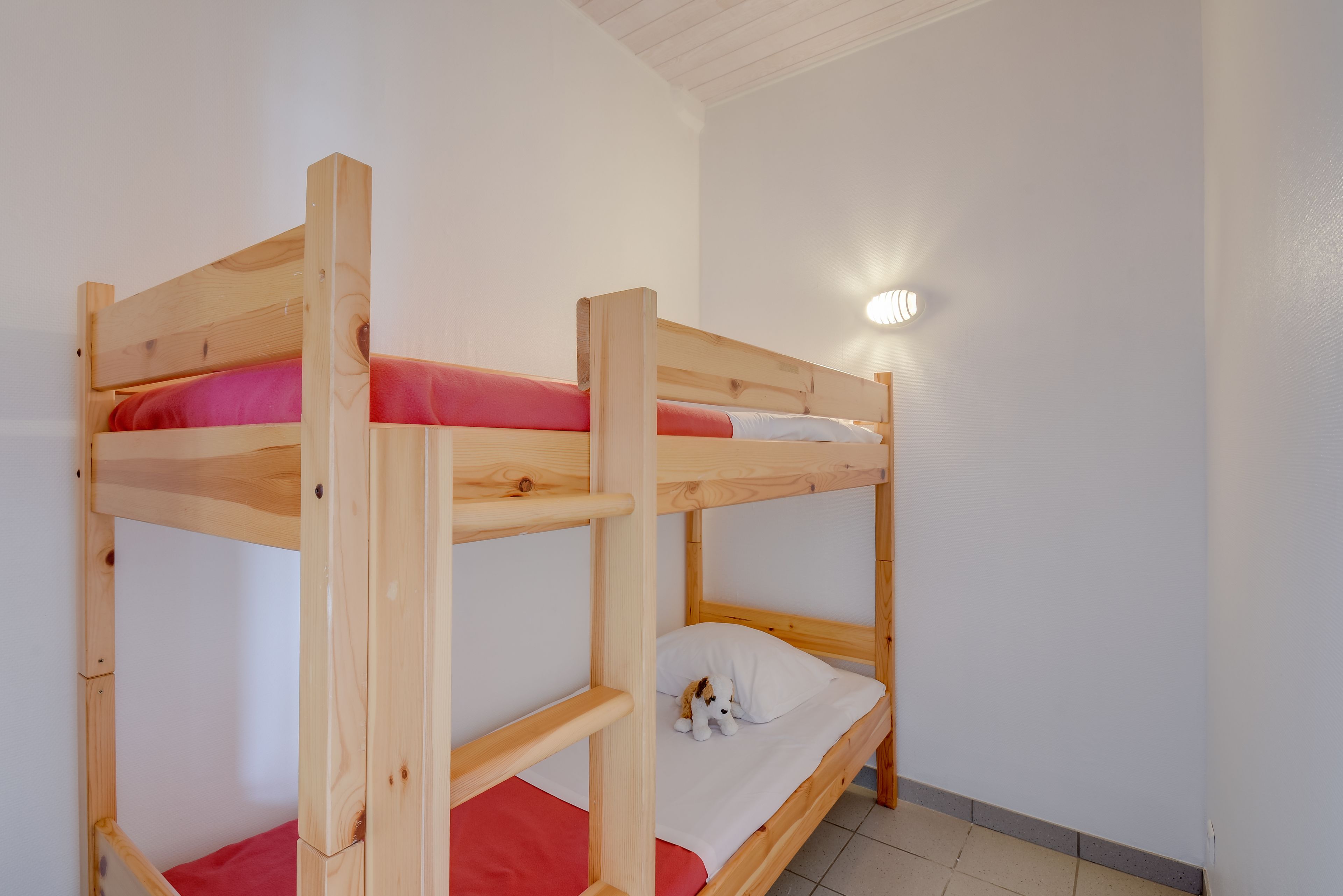 A bunk bed room with a wooden frame, a red mattress on the lower bunk, and a white mattress on the upper bunk.