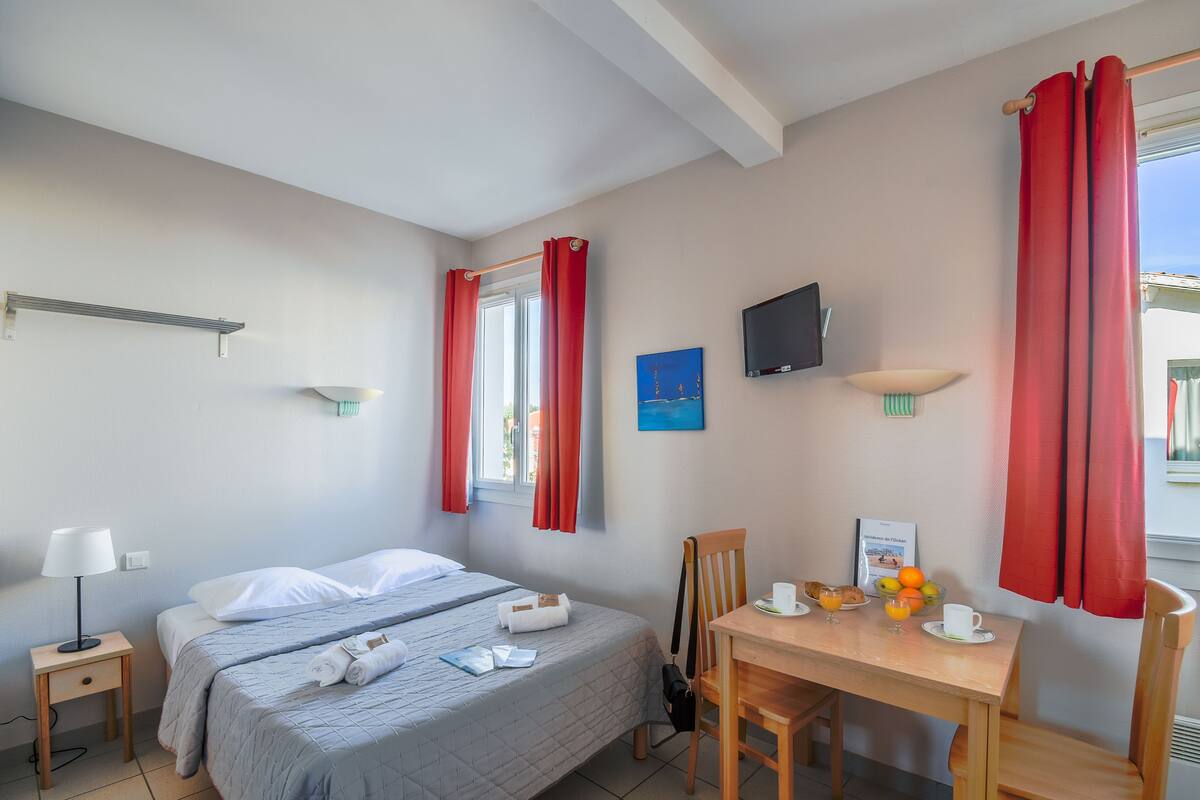 A hotel room with two beds, a desk with breakfast, a TV, and red curtains.